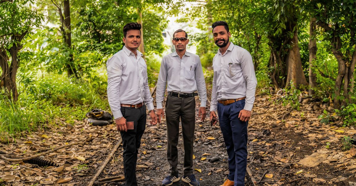 Three men in dress shirts pose confidently on a forest pathway, surrounded by lush greenery.